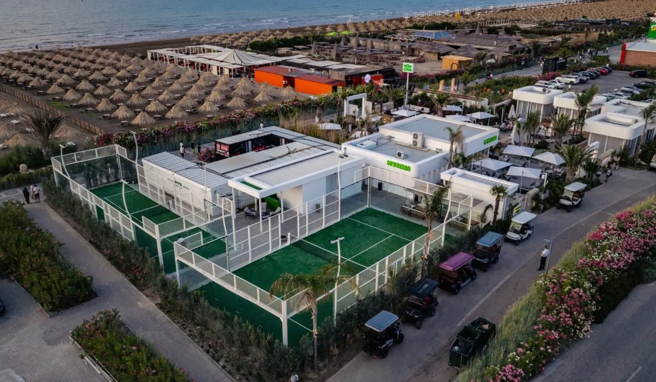 Yuxarıdan Sea Breeze-in çimərlik xətti: saman çətirlər, suyun yanında kabanalar, padel kortları və kafelərin ağ pavilyonları